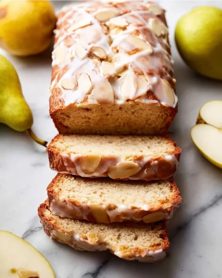 Sliced baked pear bread drizzled with almond glaze on a wooden platter